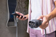 © Wavebreak Media - Holding smartphone and electric car charger, man preparing to charge vehicle
