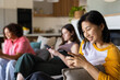 © Wavebreak Media - Using smartphones, three women friends relaxing on couch in living room