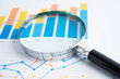 © Pakawadee - Magnifying glass on graph. Finance business and trading.