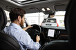 © sofiko14 - Businessman sits inside car while test driving vehicle in dealership showroom experiencing new car features steering automobile checking dashboard