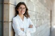 © senyumanmu - Young smiling business university student standing against college campus wall with arms crossed