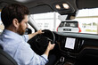 © sofiko14 - Professional man driving modern car, evaluating purchase, technology, comfort, safety. Businessman inside car dealership showroom test driving vehicle, exploring features.