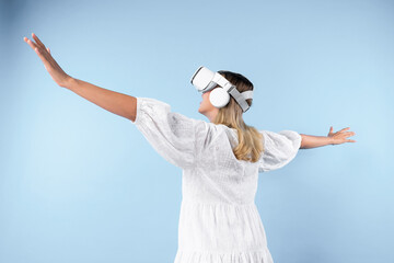 Sticker - Back view of happy girl enter metaverse while spread arms with relax at blue background. Excited woman enjoy playing game by using VR goggles with blue background. Innovation technology. Contraption.