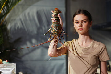 Sticker - Young woman holding a live lobster in her hand while standing in front of a kitchen