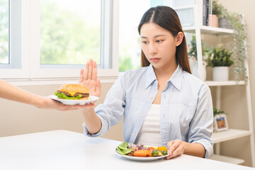 Wall Mural - Diet concept, asian young woman hand reject eat burger, hamburger on plate, push out or deny to eat fast, junk food choose green vegetable salad, girl eat low fat for good healthy, getting weight loss