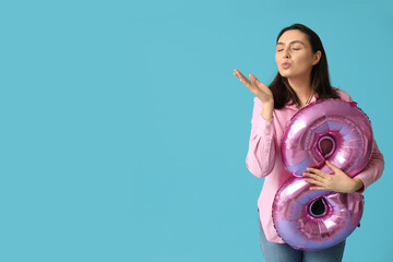 Wall Mural - Beautiful young woman with pink air balloon in shape of figure 8 blowing kiss on blue background. International Women's Day