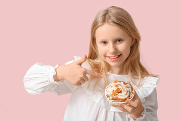 Canvas Print - Cute little girl pointing at tasty cinnamon bun on color background