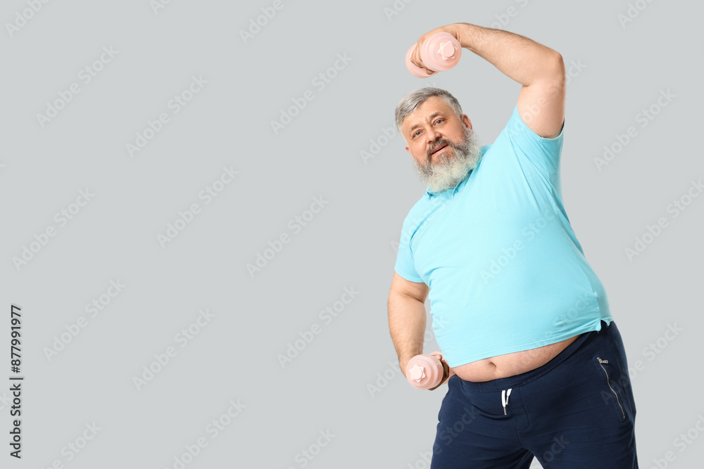 Overweight happy mature man with dumbbells on grey background. Weight loss concept