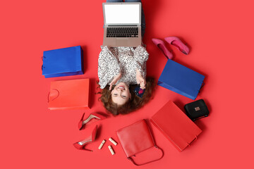 Poster - Beautiful young woman with modern laptop, stylish high heels, lipsticks and shopping bags on red background