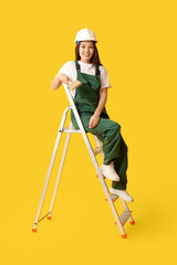 Wall Mural - young female painter with brush sitting on ladder against yellow background