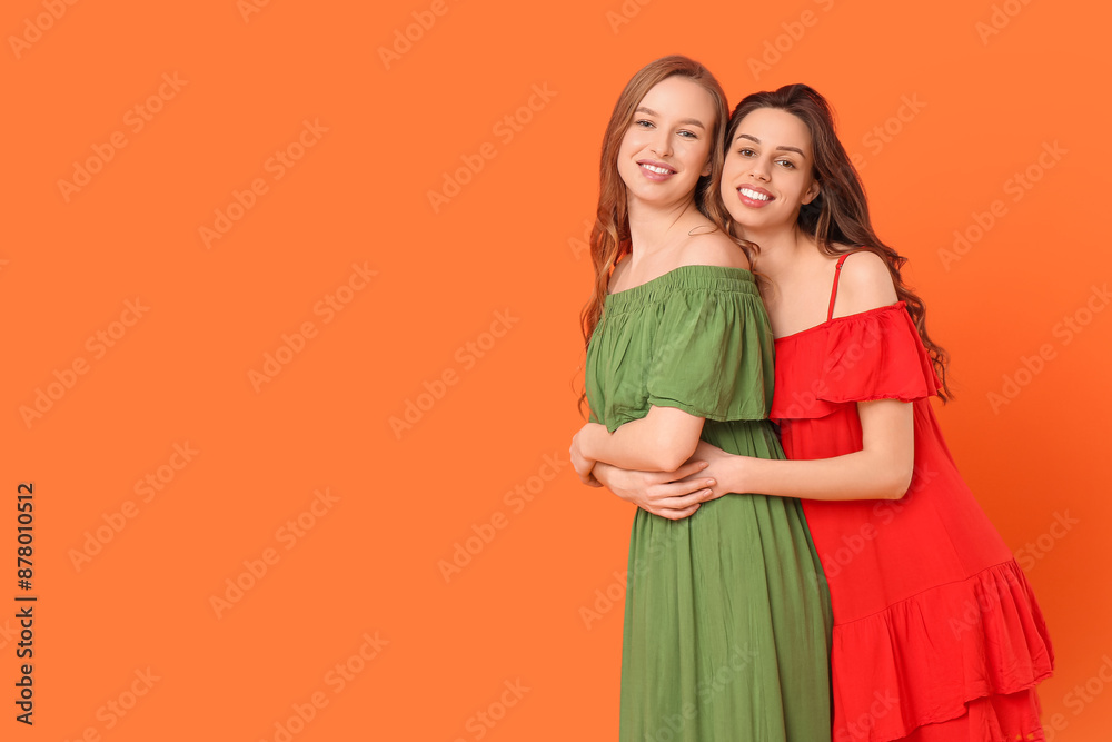 Beautiful young sisters hugging on orange background