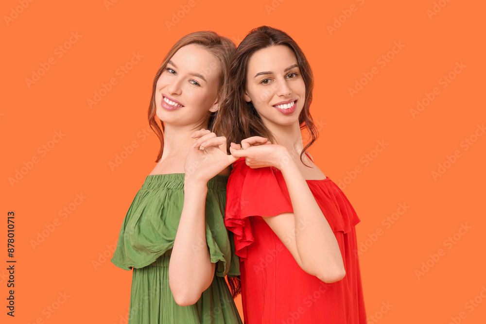 Beautiful young sisters holding with little fingers on orange background