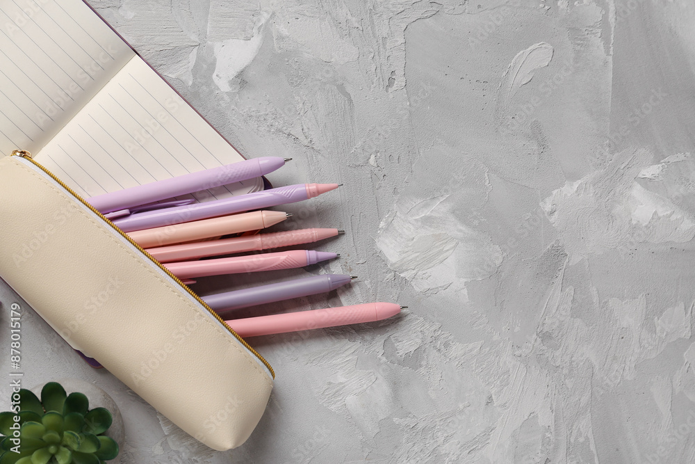 Pencil case with colorful pens, flowerpot and notebook on grey grunge background