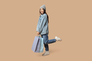 Sticker - Fashionable young Asian woman in stylish denim clothes with shopping bags on brown background