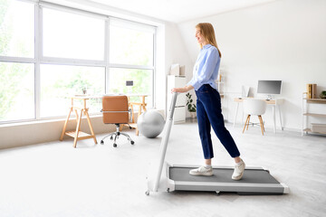 Poster - Young businesswoman training on treadmill in office