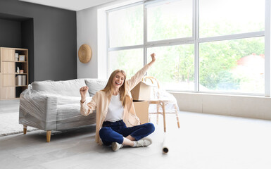 Wall Mural - Happy young woman with stretch wrap sitting in room on moving day