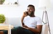 © Prostock-studio - Handsome millennial African American businessman working from home, sitting on couch, using laptop and talking on phone
