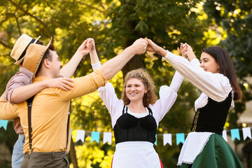 Canvas Print - Young people in traditional German clothes dancing outdoors. Octoberfest celebration