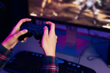 Aufkleber - This is a photo of a persons hands holding a video game controller, with a computer monitor in the background displaying an action game. The person is immersed in the game, focused on the screen.