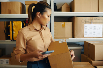 Woman using her mobile phone to check barcode on parcel