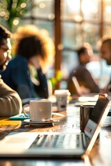 Coffee cups and laptops on a wooden table in a shared workspace with people collaborating. Freelancing, coworking space, creative team, remote work, casual meeting, productivity concept.