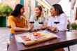 © Xavier Lorenzo - Three happy diverse women having fun together enjoying red wine at restaurant. Focus on wooden board with cheese and ham.