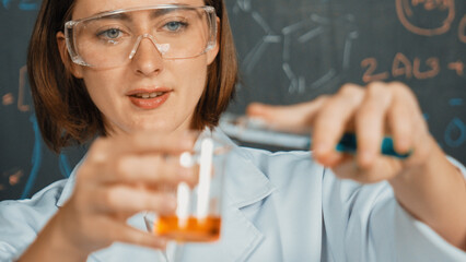 Poster - Closeup of young beautiful teacher focus on mixing chemical liquid at laboratory. Skilled scientist doing an experiment by inspect colored solution while standing in front of blackboard. Erudition.