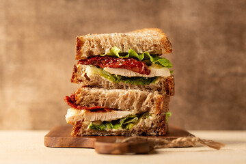 Canvas Print - Chicken breast sandwich with whole wheat bread, ricotta cheese, lettuce, and sun dried tomatoes. On a wooden board, brown background.