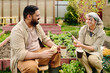© pressmaster - Cheerful mature couple in workwear looking at one another and having chat at coffee break while sitting among flowerbeds in the garden