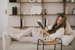 © polinaloves - Young woman reading book and drinking tea, sitting on sofa in a cozy living room.