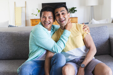 Biracial man and Middle Eastern man share a joyful moment during a video call on the couch at home