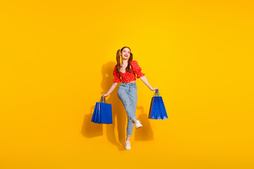 Wall Mural - Full length photo of lovely young lady hold shopping bags walking dressed stylish red retro garment isolated on yellow color background