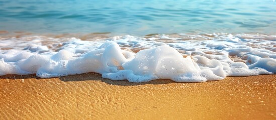 Poster - Close-up view of a sea wave, highlighting white foam on a golden sandy beach by the blue ocean; ideal summer backdrop with ample copy space for images, featuring selective focus.
