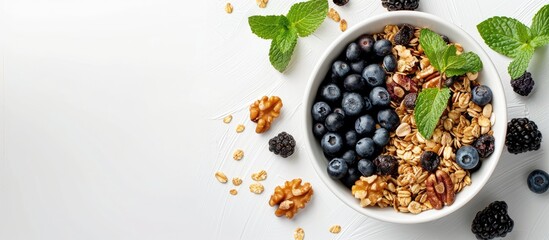 Wall Mural - Top view of a white bowl filled with homemade granola, muesli, cereals, blackberries, blueberries, nuts, honey, and mint on a white background, with copy space image.