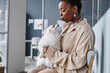© Seventyfour - Side view portrait of young happy African American pet owner in vet clinic waiting room cuddling with her dog giving kiss, copy space