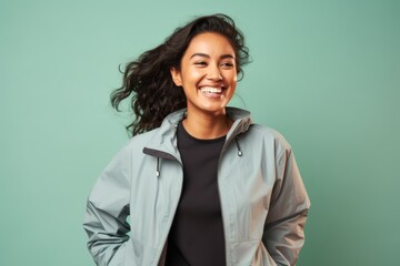 Poster - Portrait of a grinning indian woman in her 20s wearing a functional windbreaker while standing against pastel or soft colors background