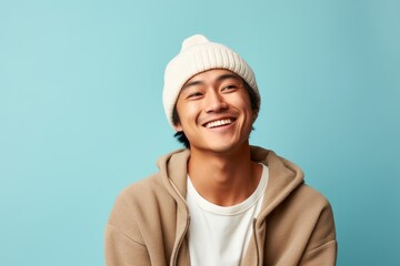 Poster - Portrait of a cheerful asian man in his 20s donning a warm wool beanie in pastel or soft colors background