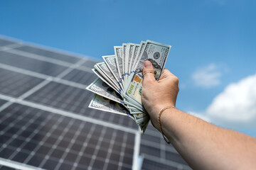 Wall Mural - male hand hold hundred dollar against solar station, saving concept