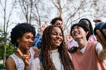 Wall Mural - Diverse friends smiling and taking a selfie outdoors with trees in the background.