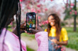 © Koldo_Studio - Close-up of African woman being photographed among pink blossoms in a park.