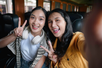 Two young women happily taking a selfie on a train, showing the peace sign and capturing the moment together