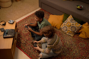 High angle view of two teenage boys sitting on retro carpet and playing retro video games, showing vintage gaming console and controllers