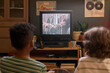 © pressmaster - Back view of two kids sitting on floor watching TV showing horror movie about zombies in cozy retro living room with plants and posters on wall, and old-fashioned gaming console below TV screen