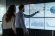 © Iftikhar alam - A man and woman stand in front of a large screen, analyzing financial charts together in a professional setting, Colleagues analyzing financial charts on a large screen