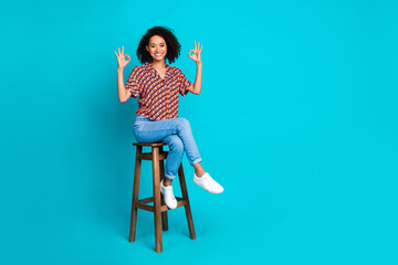 Wall Mural - Photo of positive girl sit chair make okay symbol isolated cyan color background