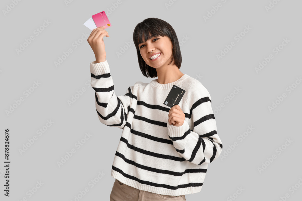 Happy young woman with credit cards on grey background