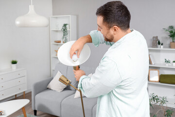 Wall Mural - Young man changing light bulb in standard lamp at home