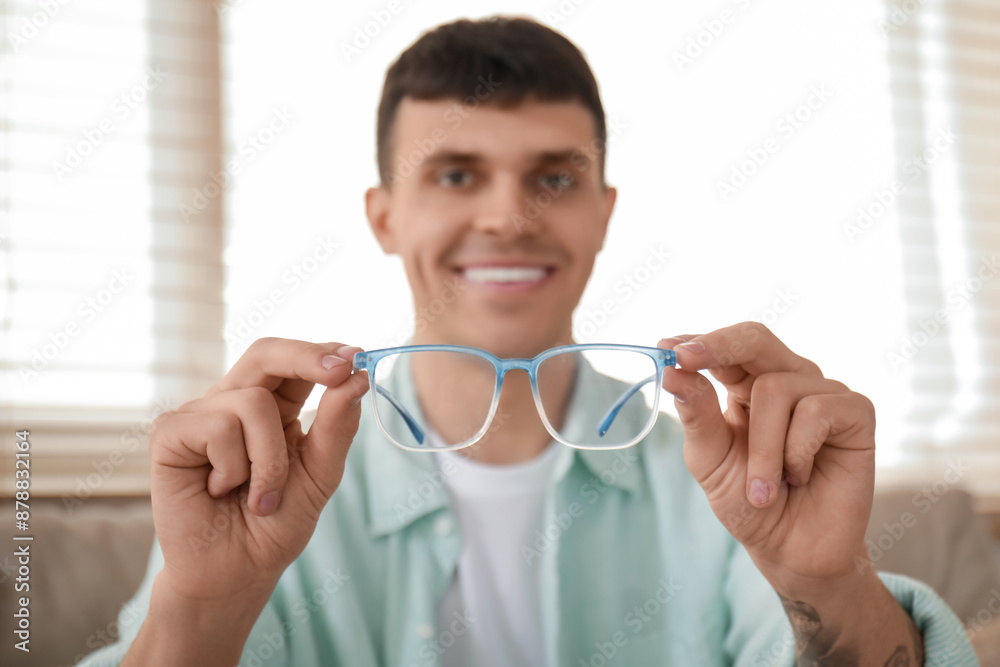 Handsome happy young man with new stylish eyeglasses at home
