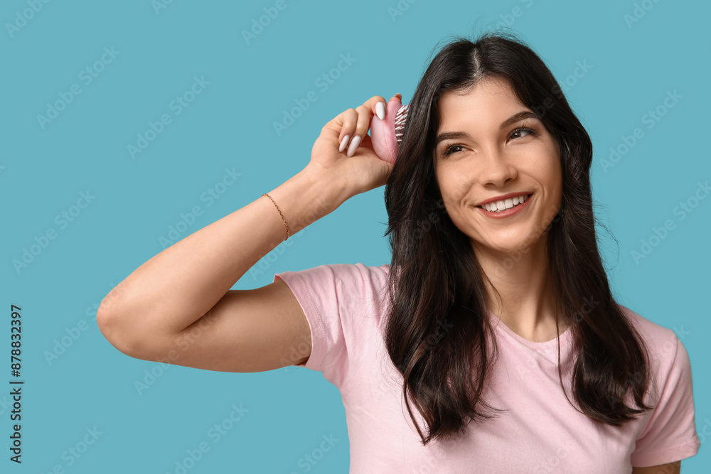 Pretty young woman brushing her hair on blue background