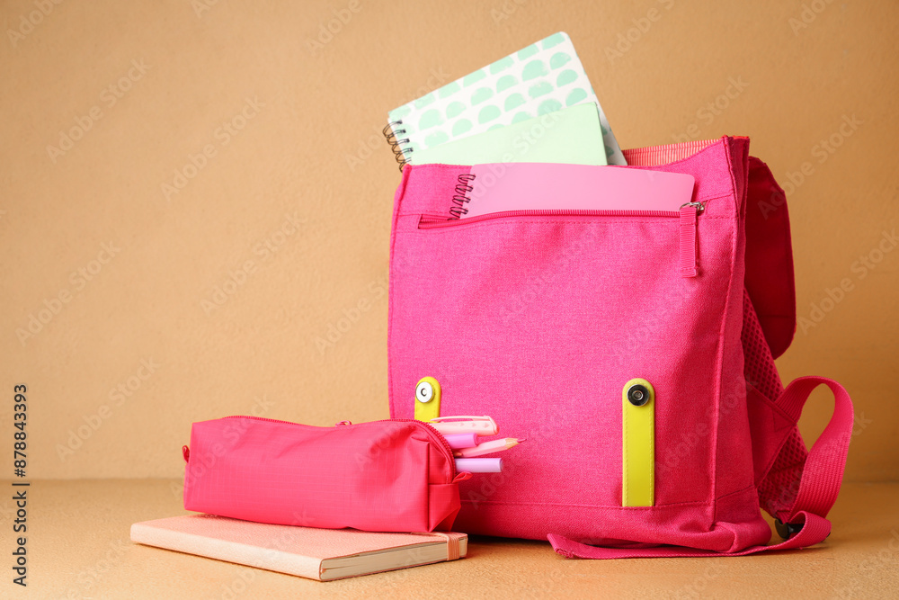 Pink backpack with notebooks and pencil case on table against beige wall